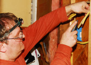 Jonathan Murphy of Hot & Cold Electric rewires behidn the bathroom wall, where he replaced a non-GFCI, code-violating dual outlet dependent on a light switch with a four-outlet, GFCI unit.